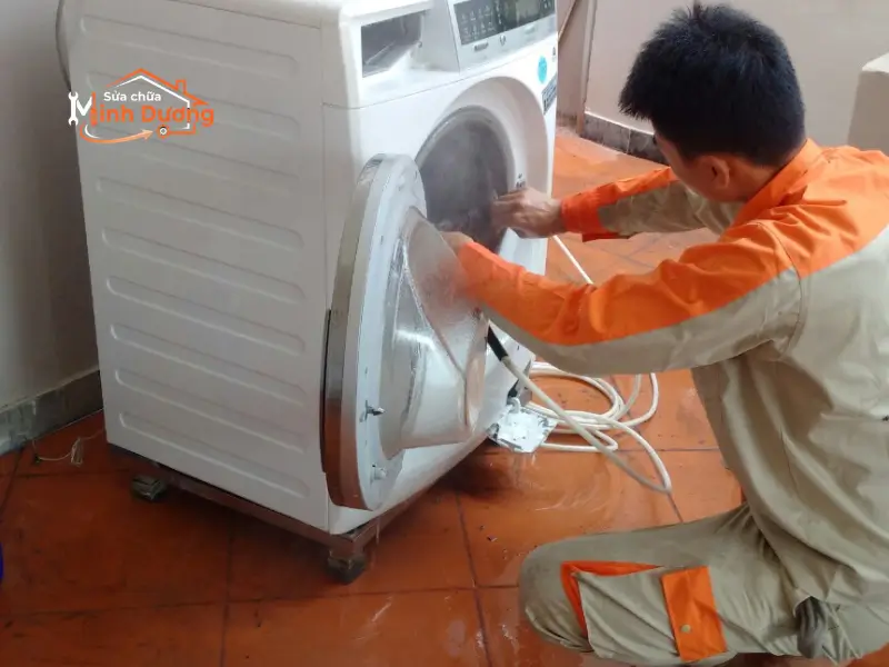 Thợ vệ sinh máy giặt lồng ngang của Minh Dương Fix đang sử dụng máy phun áp lực cao để đánh bay nấm mốc và cặn bẩn tích tụ bên ngoài lồng inox Electrolux.